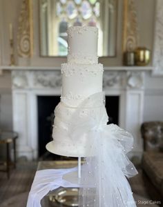 a white wedding cake sitting on top of a table in front of a fire place