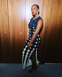 a woman standing in front of a wooden wall wearing black and white polka dot print dress