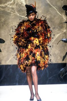 a woman is walking down the runway in a dress made out of fire and black feathers