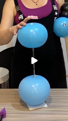 a woman holding two blue balloons on top of a table