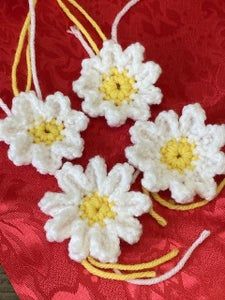 three crocheted flowers are sitting on a red cloth with yellow and white thread