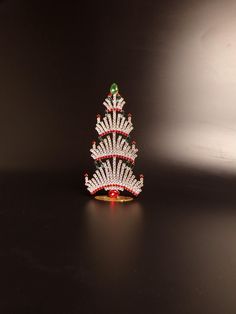 a small christmas tree made out of beads on a black surface with white and red trim