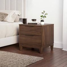 a white bed sitting next to a wooden nightstand on top of a hard wood floor