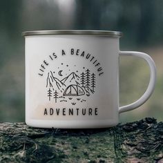 a white enamel mug with the words life is a beautiful adventure on it sitting on a tree stump