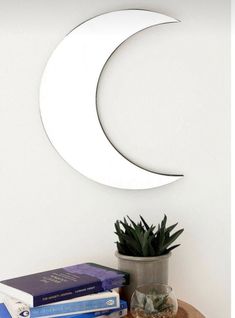 a table topped with books and a plant next to a moon shaped wall mounted mirror