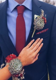 a man in a suit and red tie with two succulents on his lapel