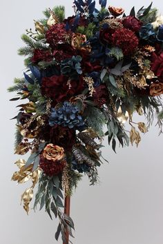 a bouquet of flowers and greenery on top of a wooden stick in front of a white wall