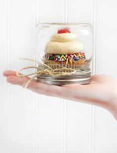 a hand holding a cupcake under a glass dome