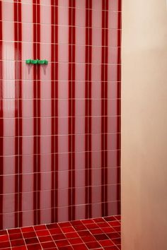 a bathroom with red tiles and green handles on the shower door is seen in this image