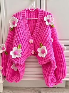 a pink knitted sweater with flowers on the front and back, hanging from a hook