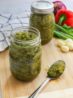 two jars filled with pesto on top of a wooden cutting board next to vegetables