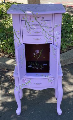 a purple cabinet with flowers painted on the front and sides, sitting next to a tree