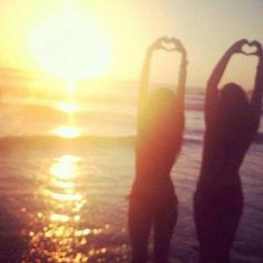 two people standing on the beach with their arms in the air making a heart shape