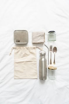 the contents of a travel bag laid out on top of a white sheet with utensils