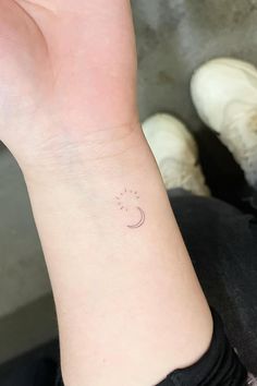 a woman's wrist with a small sun and moon tattoo on her left arm