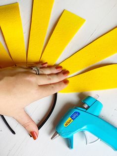 a woman's hand holding a yellow piece of paper next to scissors and glue