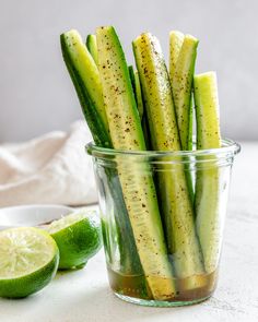 pickled cucumbers in a glass container with limes and salt on the side