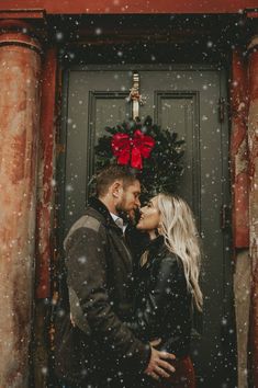 a man and woman kissing in front of a green door with snow falling on them