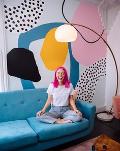 a woman with pink hair sitting on a blue couch in front of a colorful wall