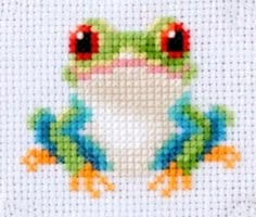 a cross stitch frog sitting on top of a white surface with red eyes and green legs