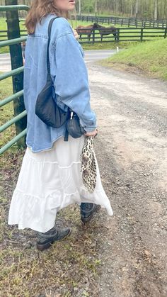 a woman standing in front of a fence holding a leopard print purse and wearing a denim jacket