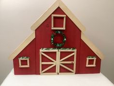 a red barn with a wreath on the door and windows in the roof is made out of wood