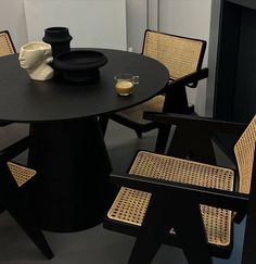 a black table with chairs and a vase on it in front of a white wall