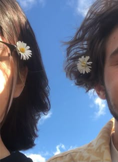 two people with flower in their hair looking up at the sky and clouds behind them