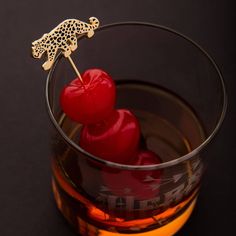 a glass filled with liquid and two red cherries on top of each other in front of a black background