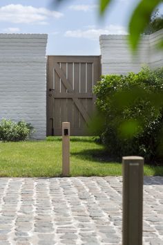 a brick walkway in front of a white house with a wooden gate on the other side