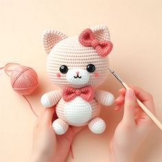 a hand holding a crocheted teddy bear next to a ball of yarn and knitting needles