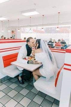 a bride and groom sitting at a table in a diner kissing each other's foreheads