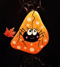 an orange and white rock with a black spider painted on it's face next to a maple leaf