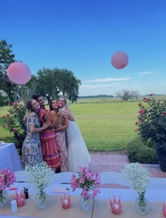 three women standing next to each other in front of a table with flowers and balloons