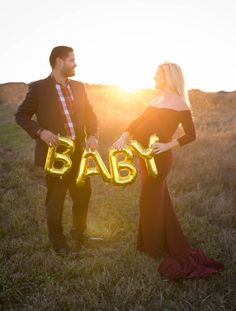 a man and woman are standing in the grass holding letters that spell out'baby '