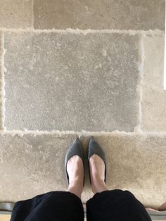 a woman's feet in high heels sitting on a stone bench next to a wall