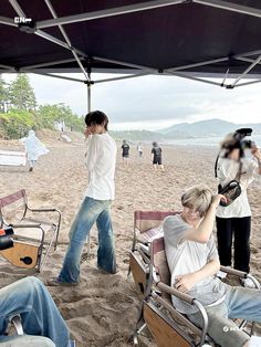 some people are sitting under a tent on the beach and one is holding a camera