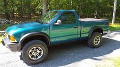 a green pick up truck parked in front of some trees