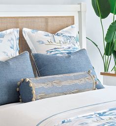 a bed with blue and white pillows on top of it next to a potted plant