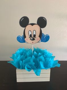 a mickey mouse cake topper sitting on top of a box filled with blue tissue