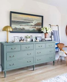 a blue dresser in a room with a painting on the wall and pictures above it