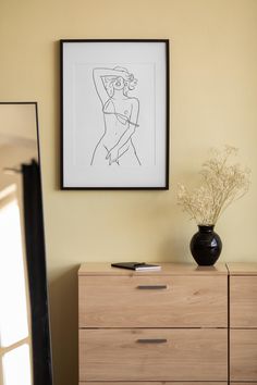 a black vase sitting on top of a wooden dresser next to a framed nude drawing