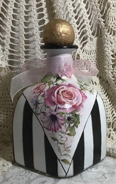 a white and black striped vase with pink flowers on it's top, sitting on a lace doily