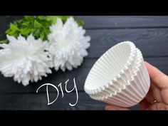 a hand holding a white cupcake liner next to some flowers on a black table