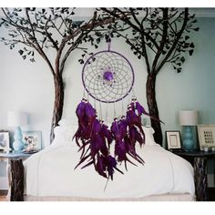 a purple dream catcher hanging from the side of a bed next to two tree branches