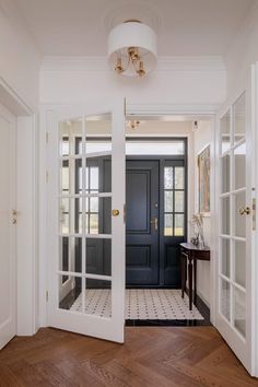 an open door leading into a hallway with wooden floors and white walls, along with two black doors