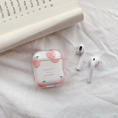 an apple airpods case sitting on top of a bed next to an open book