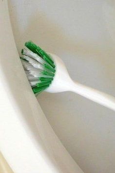 a green and white toothbrush sitting in the corner of a toilet