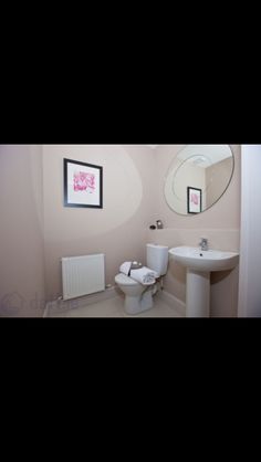 a white toilet sitting next to a sink in a bathroom under a round mirror on the wall