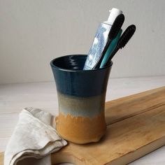 three toothbrushes in a cup sitting on a wooden tray next to a cloth